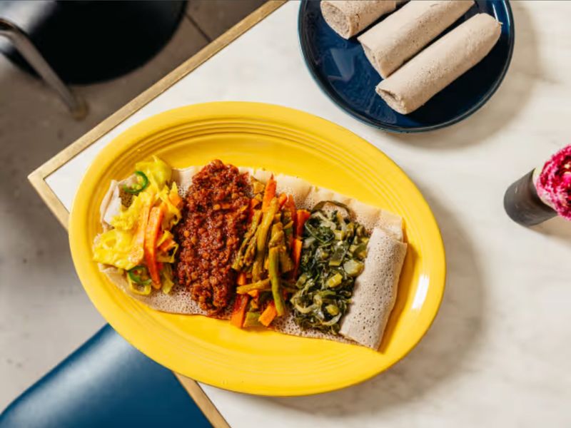 Colorful vegetarian combination platter on injera with rolled injera alongside