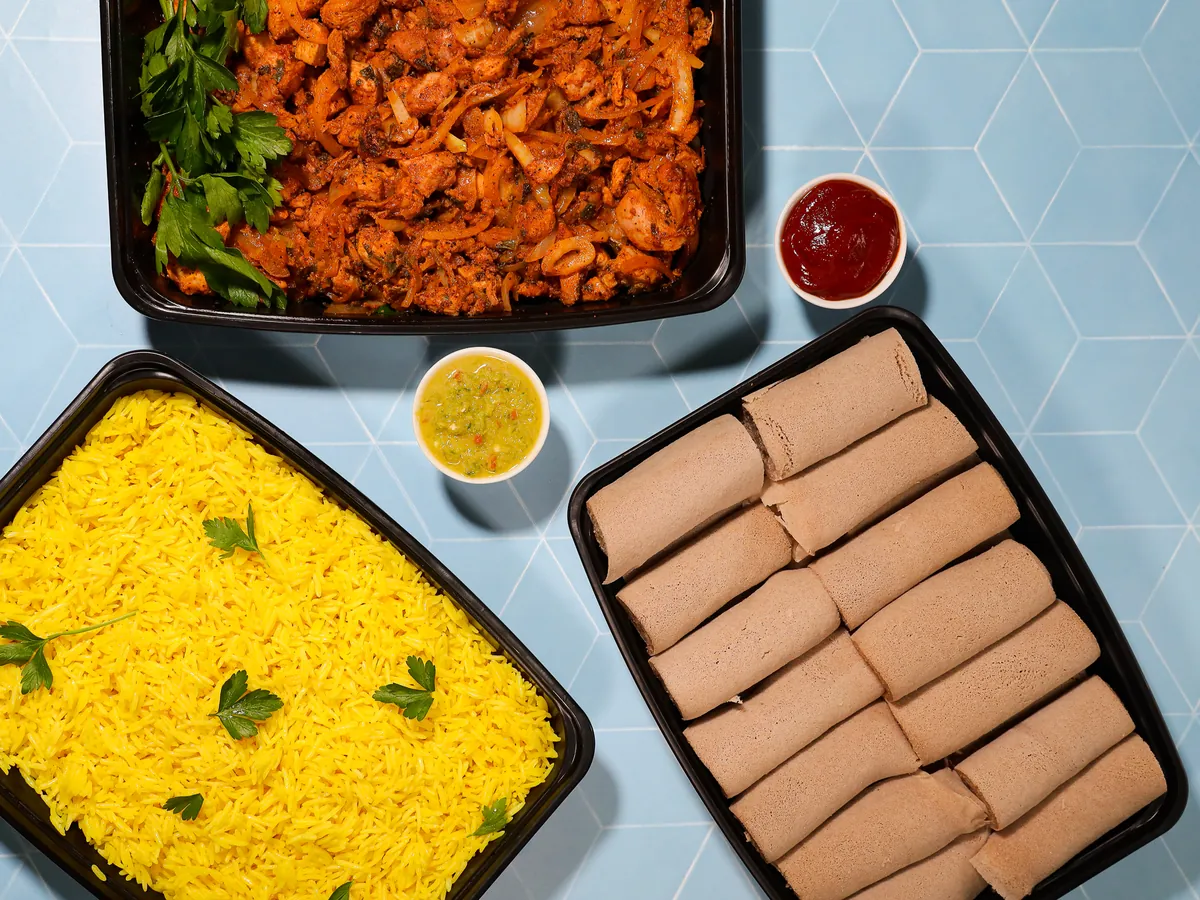 Makina Eritrean-Ethiopian catering trays for an office lunch: yellow rice, spiced chicken, rolled injera and house sauces
